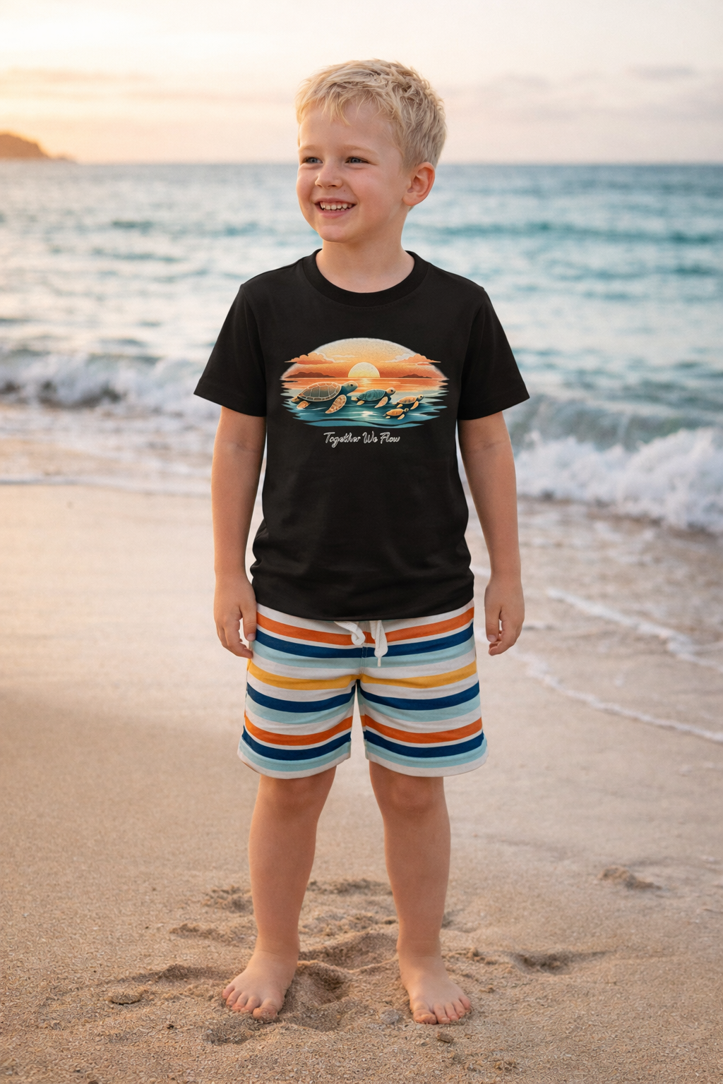 Smiling child in beach setting wearing sea turtle graphic t-shirt with sunset design and striped shorts