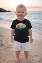 Toddler boy wearing black turtle graphic t-shirt and white shorts on beach at sunset