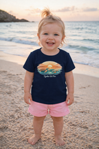 Toddler girl in navy “Together We Flow” t-shirt and pink shorts standing barefoot on beach