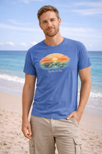 Model wearing blue turtle sunset t-shirt on sandy beach, relaxed summer vacation style