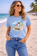 Woman wearing blue graphic t-shirt with cartoon duck skateboarding on a beach boardwalk, styled with denim jeans in a sunny coastal setting